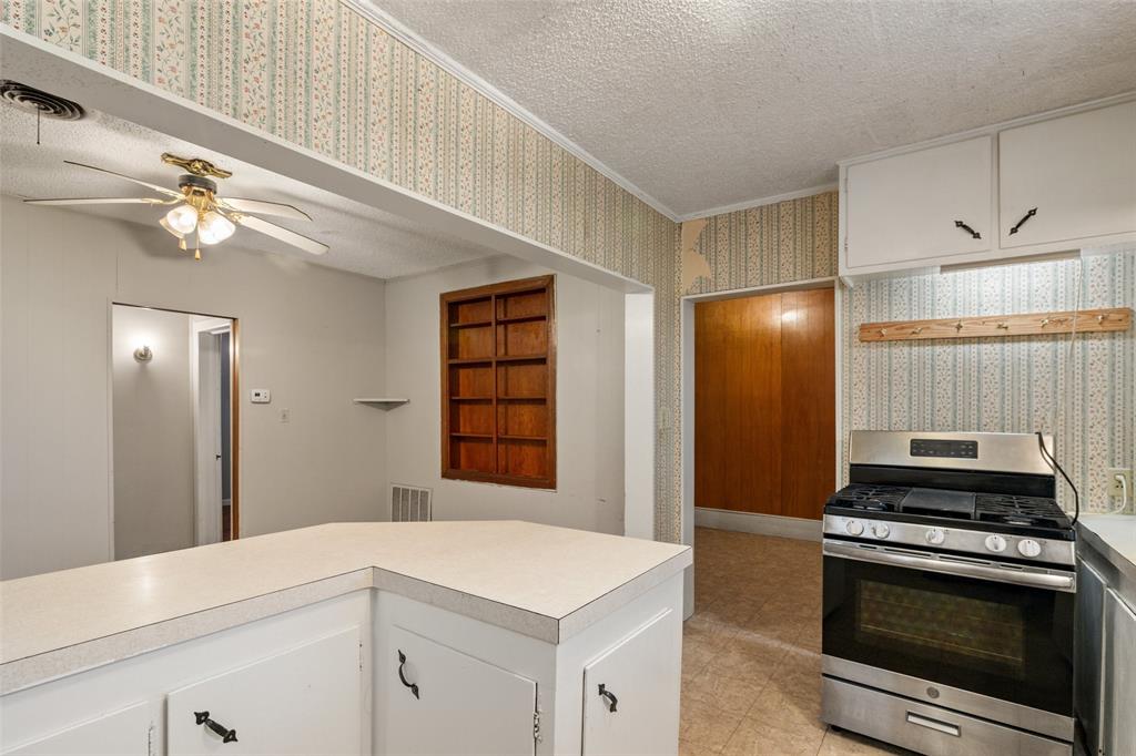 302 West Grogan Street Hamilton, TX 76531 - Photo 16 of 33 Kitchen featuring a textured ceiling, visible vents, gas range, light countertops, and wallpapered walls