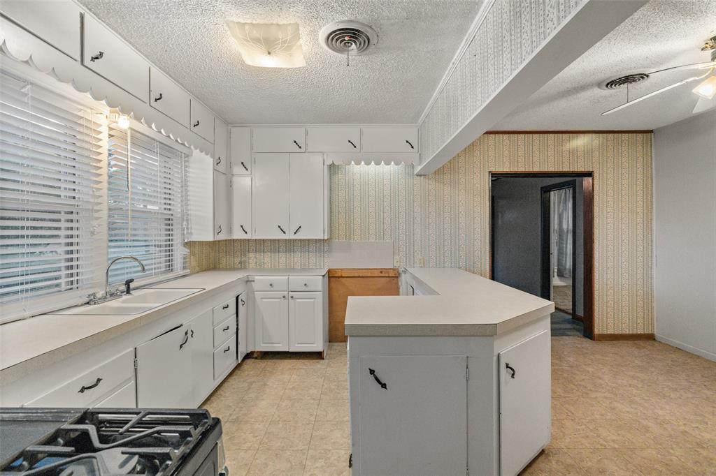 302 West Grogan Street Hamilton, TX 76531 - Photo 26 of 33 Kitchen with a textured ceiling, visible vents, a sink, light countertops, and wallpapered walls