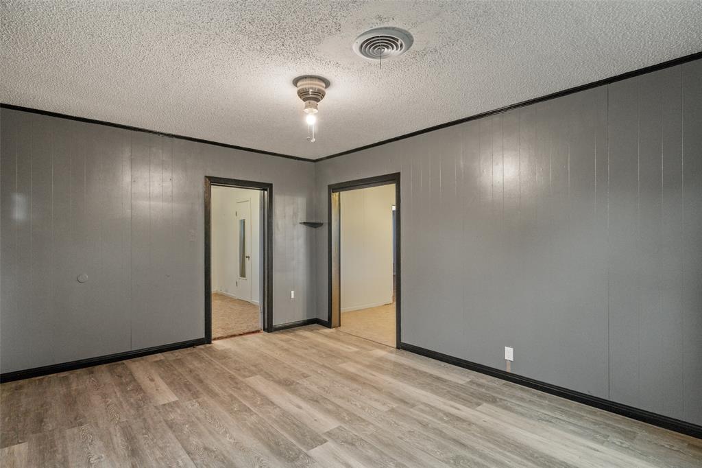 302 West Grogan Street Hamilton, TX 76531 - Photo 10 of 33 Unfurnished room with light wood-style floors, baseboards, a textured ceiling, and visible vents