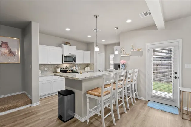a kitchen with stainless steel appliances kitchen island granite countertop a dining table chairs and white cabinets
