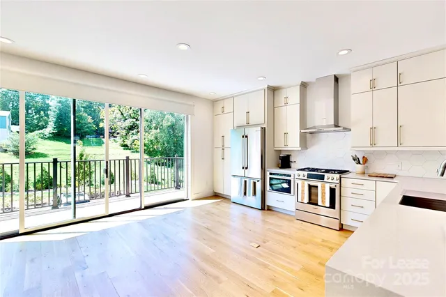 a kitchen with stainless steel appliances granite countertop a stove a refrigerator a sink and white cabinets with wooden floor