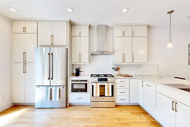 a kitchen with stainless steel appliances granite countertop a refrigerator a stove and white cabinets with wooden floor