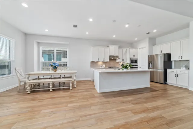a large kitchen with stainless steel appliances wooden floors and white cabinets