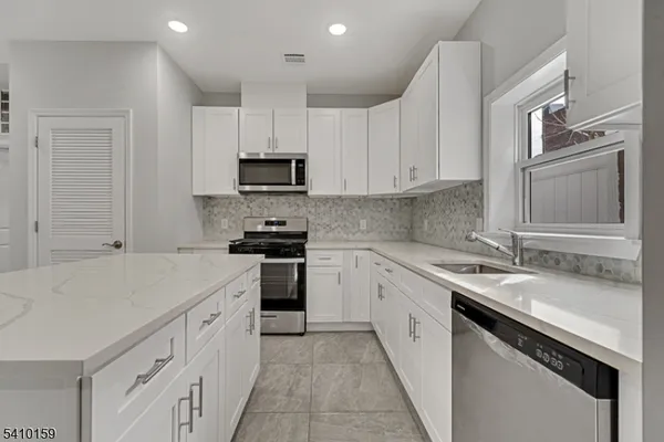 a kitchen with granite countertop a sink dishwasher stove and white cabinets