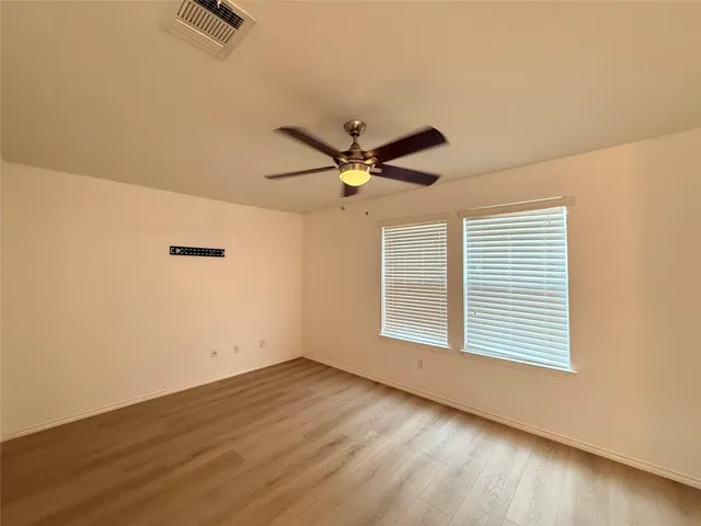 an empty room with wooden floor fan and windows