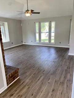 an empty room with wooden floor ceiling fan and windows