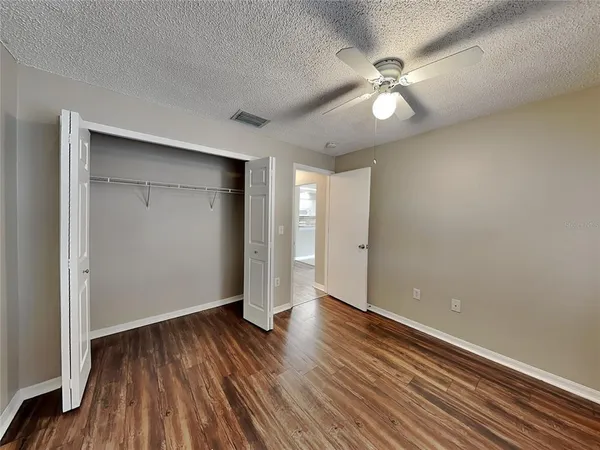 a view of an empty room with wooden floor and a ceiling fan
