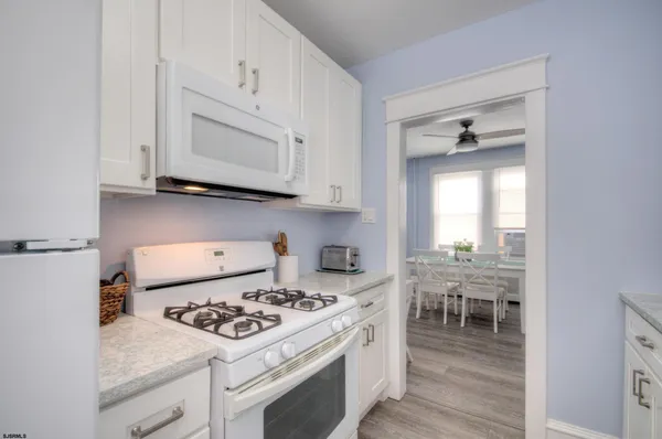 a kitchen with stainless steel appliances granite countertop a stove a sink dishwasher and white cabinets with wooden floor