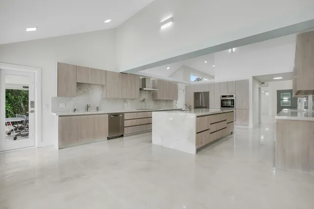 a large white kitchen with stainless steel appliances kitchen island a large counter top and a stove top oven