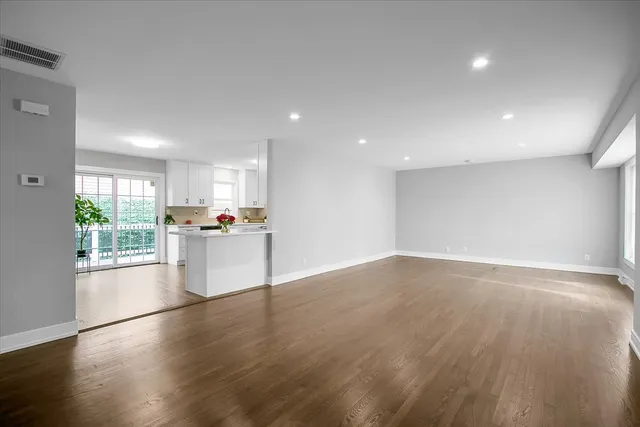 a view of empty room with wooden floor and kitchen view