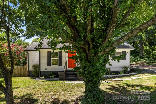 a view of a white house next to a yard with big trees