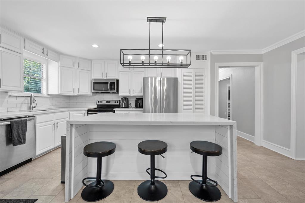 1500 South 10th Street Waco, TX 76706 - Photo 11 of 25 Kitchen with a kitchen breakfast bar, a center island, appliances with stainless steel finishes, white cabinets, and light stone countertops