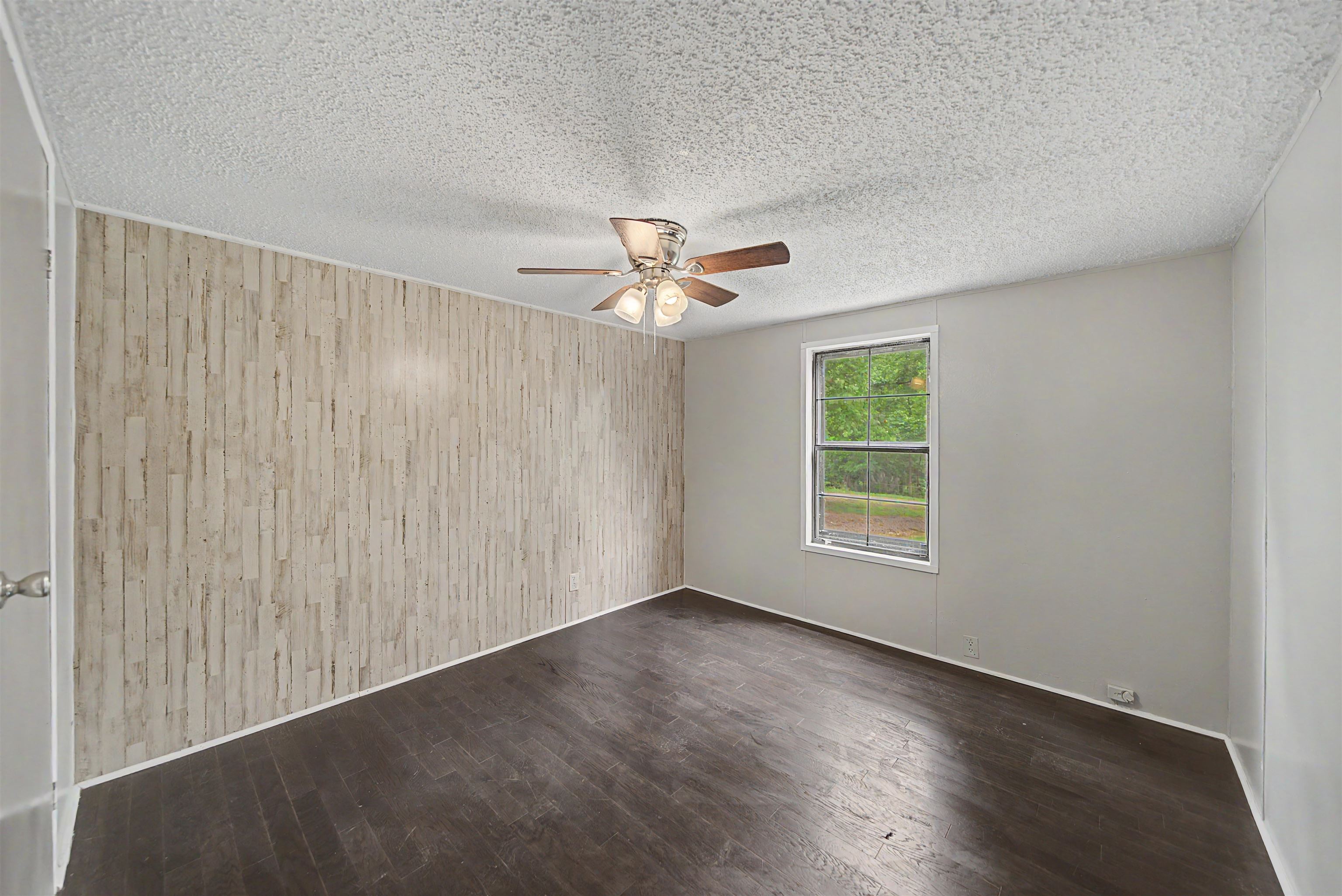 6264 45th Highway South Ramer, TN 38367 - Photo 24 of 24 Spacious room featuring dark wood-finish flooring, a textured accent wall, and neutral wall paint