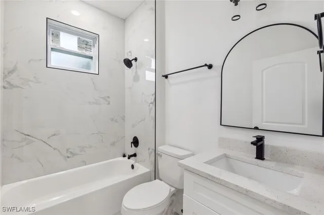 a bathroom with a granite countertop bathtub sink vanity mirror and toilet