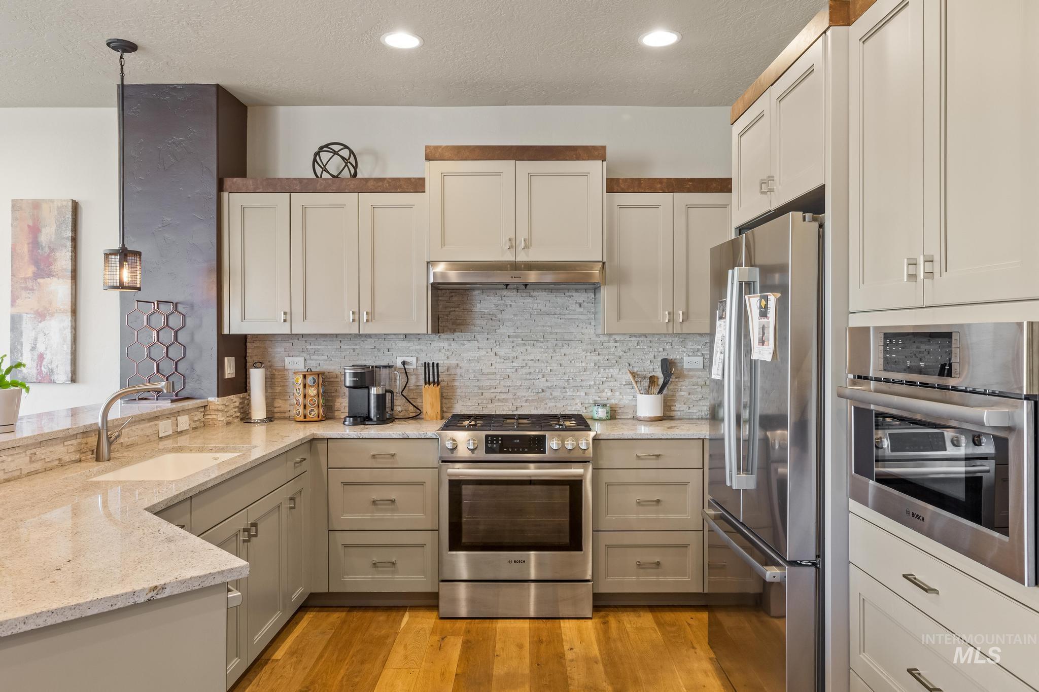 3362 East Exacta Lane Boise, ID 83716 - Photo 15 of 41 Kitchen with stainless steel appliances, light stone countertops, a textured ceiling, hanging light fixtures, and decorative backsplash