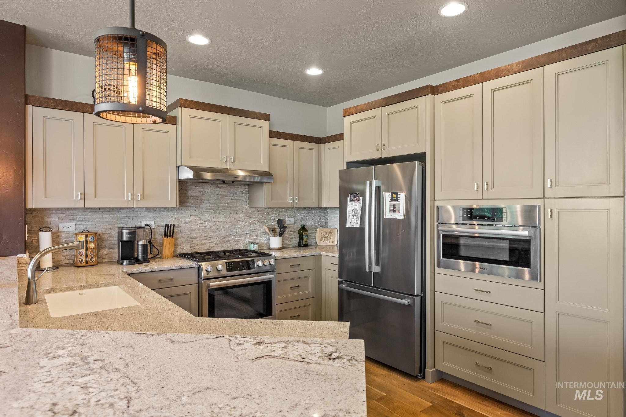 3362 East Exacta Lane Boise, ID 83716 - Photo 16 of 41 Kitchen with stainless steel appliances, light stone countertops, decorative backsplash, light wood-type flooring, and under cabinet range hood
