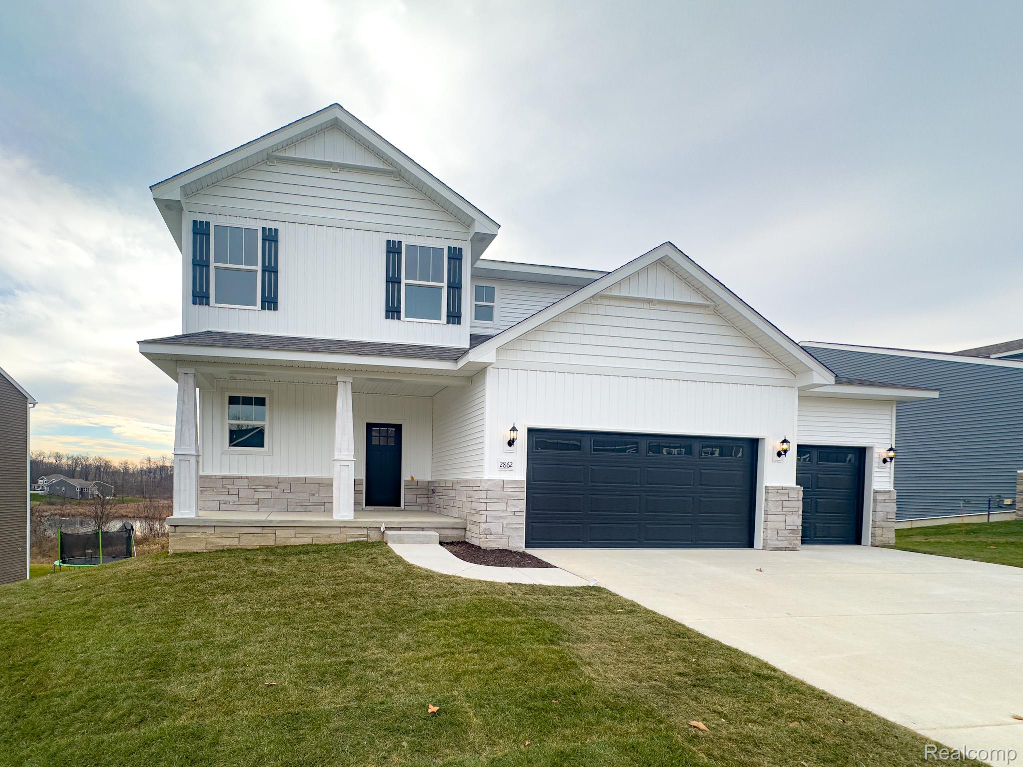 579 Round Rock (moh80) Howell, MI 48843 - Photo 1 of 42 View of front facade featuring stone siding, a porch, a garage, and a front lawn