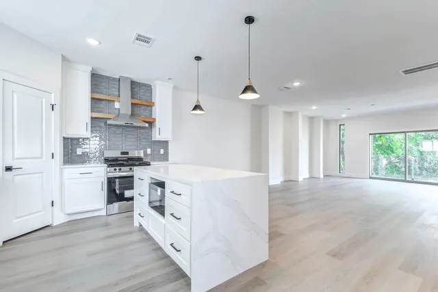 a large kitchen with stainless steel appliances granite countertop a stove a sink a refrigerator and white cabinets with wooden floor