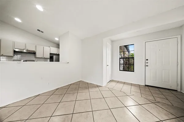 a view of an empty room with kitchen and window