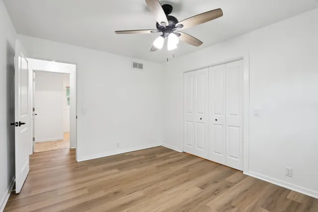 an empty room with wooden floor ceiling fan and windows