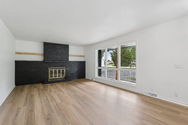 a view of an empty room with wooden floor and a fireplace