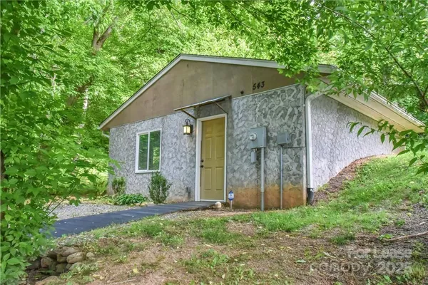 a view of a wooden house with a small yard and large trees