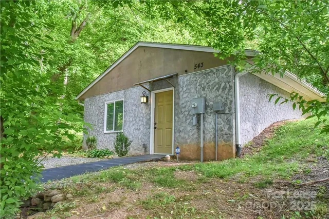 a view of a wooden house with a small yard and large trees