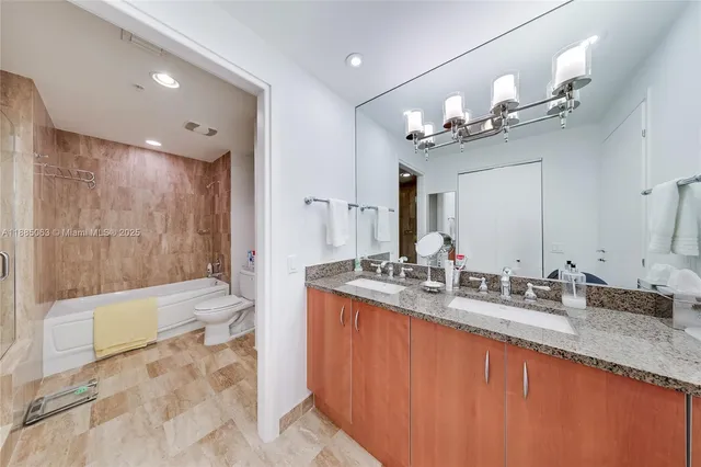 a bathroom with a granite countertop double vanity sink a toilet a mirror and shower