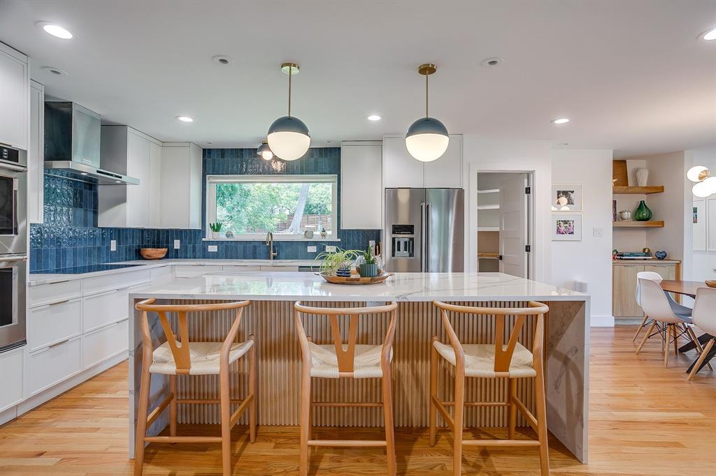 6700 Fortune Road Fort Worth, TX 76116 - Photo 7 of 40 Modern kitchen with a large central island, white cabinetry, integrated stainless steel appliances, a blue tile backsplash, and wood-finish flooring
