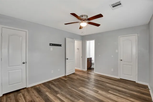 an empty room with wooden floor ceiling fan and windows