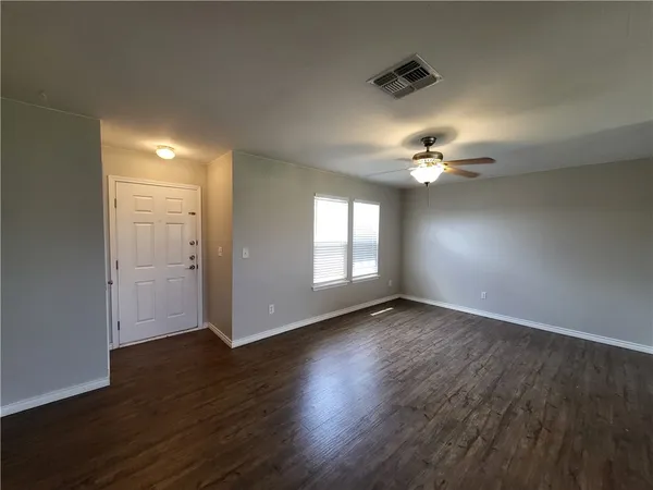 a view of an empty room with wooden floor and a window