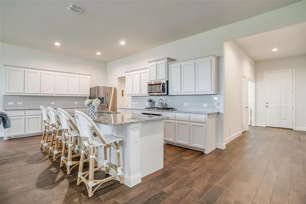 a kitchen with stainless steel appliances granite countertop a stove top oven a sink a refrigerator and white cabinets