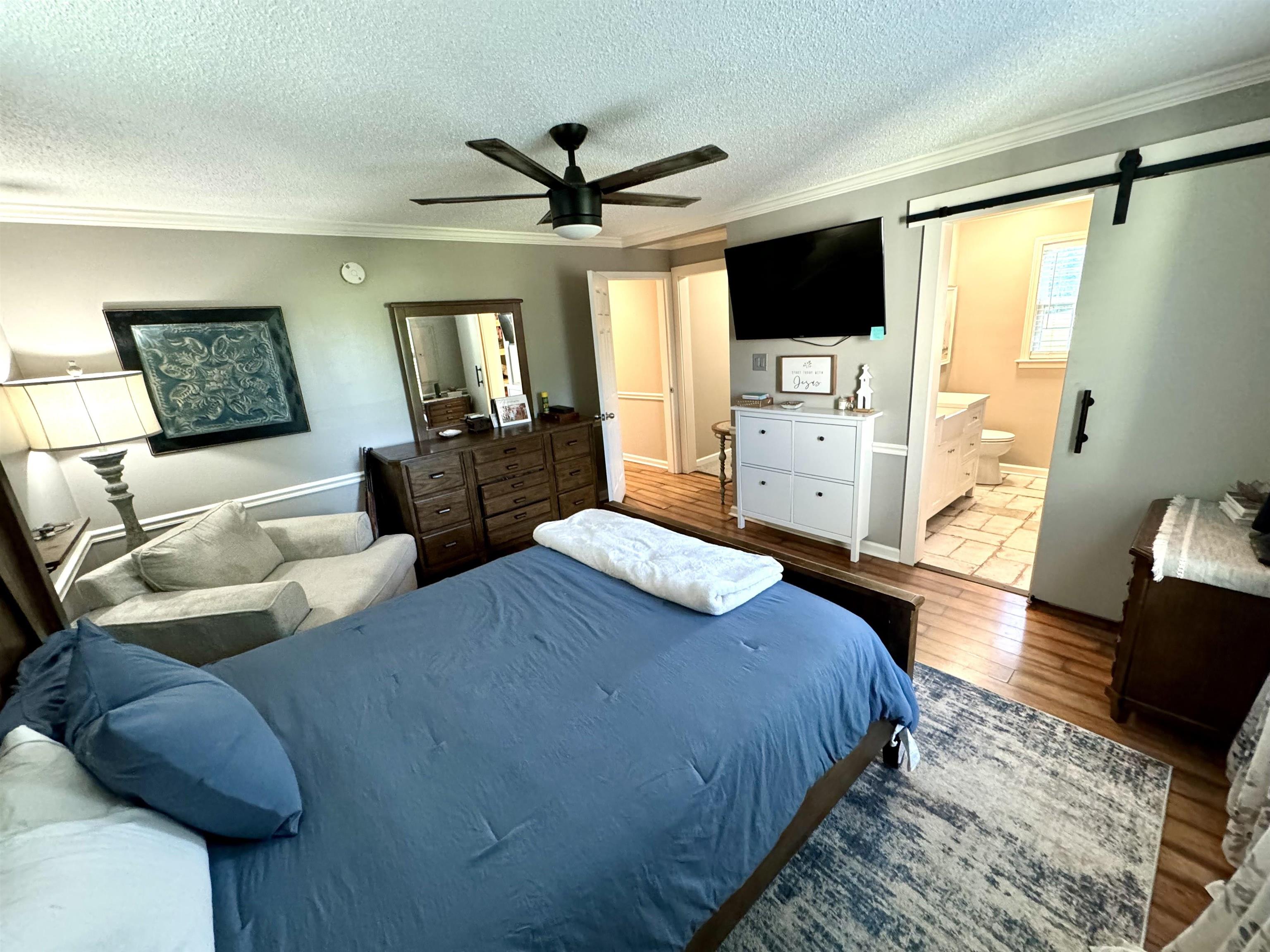 3312 Old Memphis Road Covington, TN 38019 - Photo 24 of 32 Bedroom featuring a textured ceiling, a barn door, ceiling fan, wood-type flooring, and ensuite bath