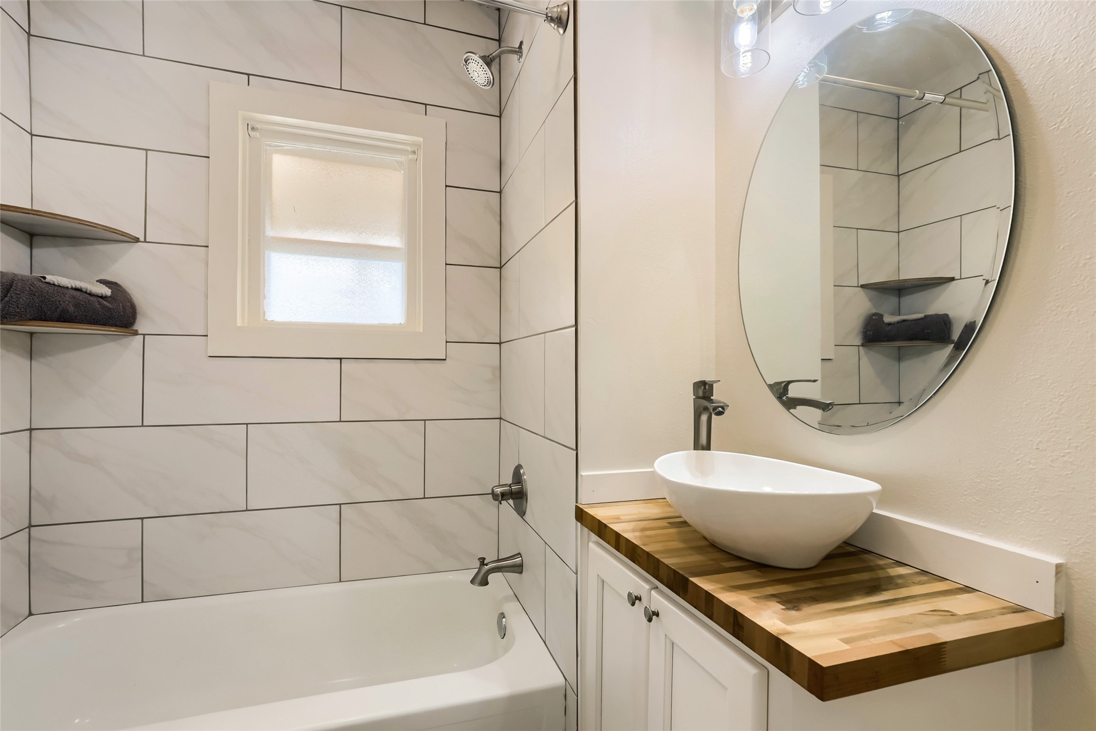 208 North Ave B Elgin, TX 78621 - Photo 24 of 29 Bathroom 2 features a modern design with subway tile walls, a sleek bathtub, and a stylish round mirror above a vessel sink on a wooden countertop. Natural light filters through a frosted window.