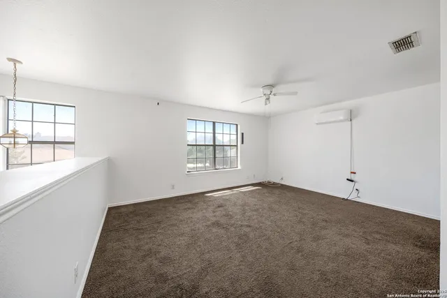 an empty room with chandelier fan and windows
