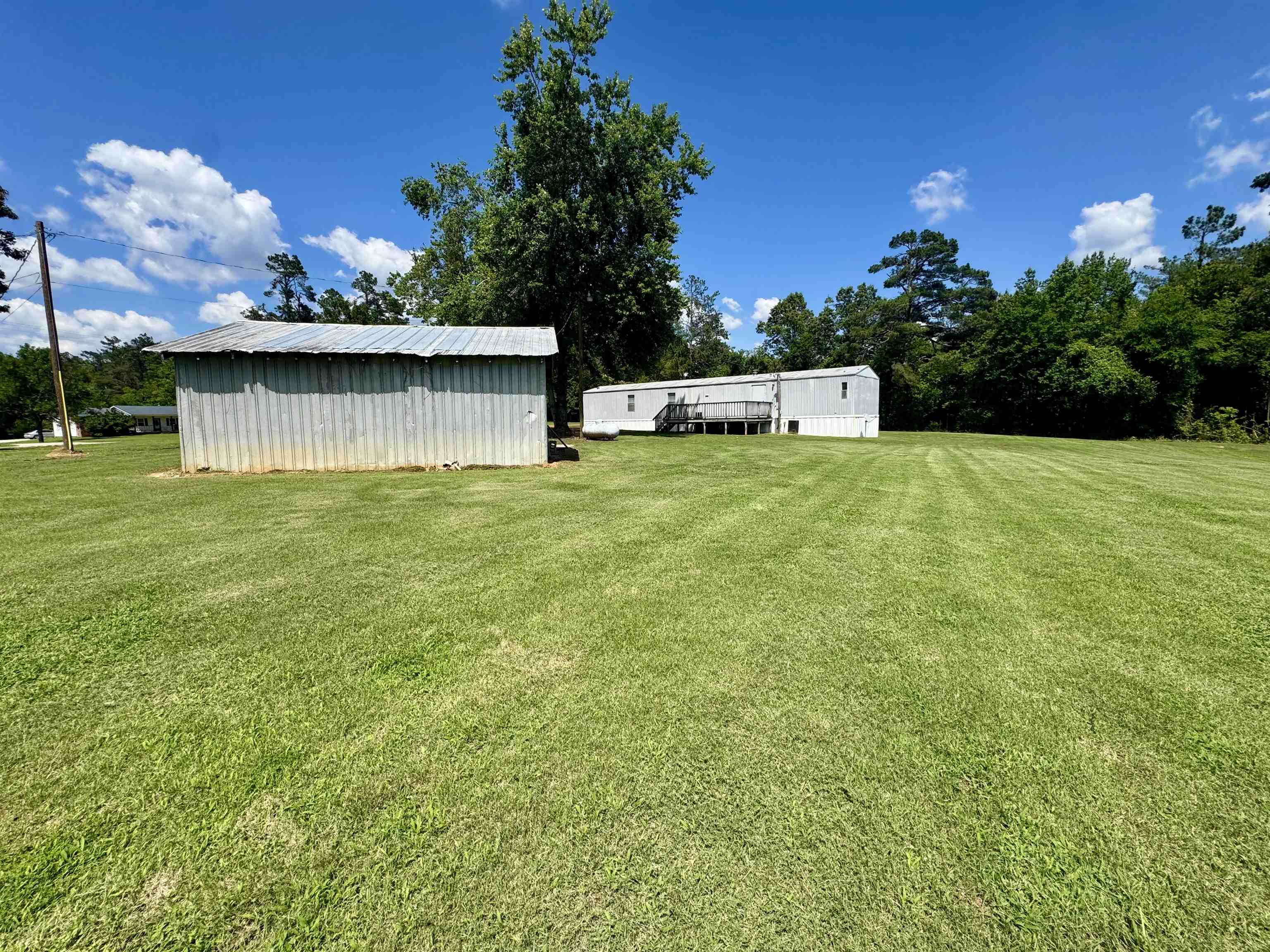 2511 Watkins Road Michie, TN 38357 - Photo 40 of 40 Expansive grass lawn featuring a corrugated metal outbuilding and a manufactured home with a wooden deck