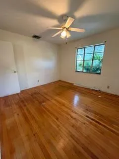 an empty room with wooden floor fan and windows