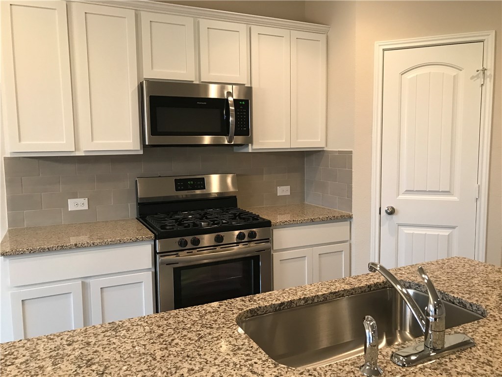 4313 Buffalo Ford Road Georgetown, TX 78628 - Photo 19 of 36 a kitchen with granite countertop a sink a stove and microwave