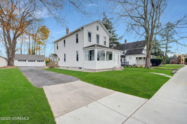 a view of a white house next to a yard with big trees