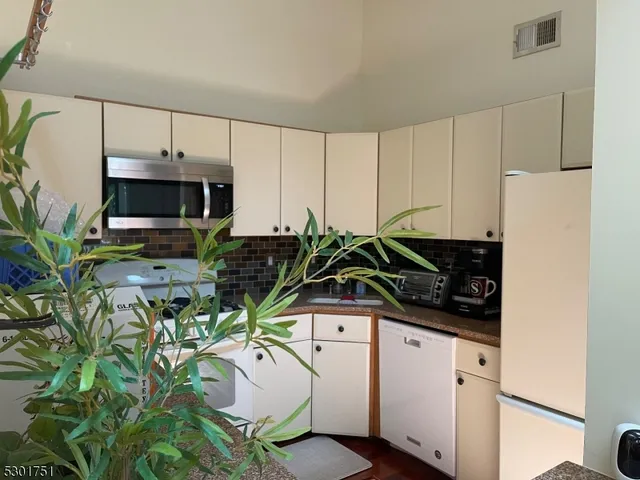 a white kitchen with stainless steel appliances a sink a stove a microwave a potted plant and a window