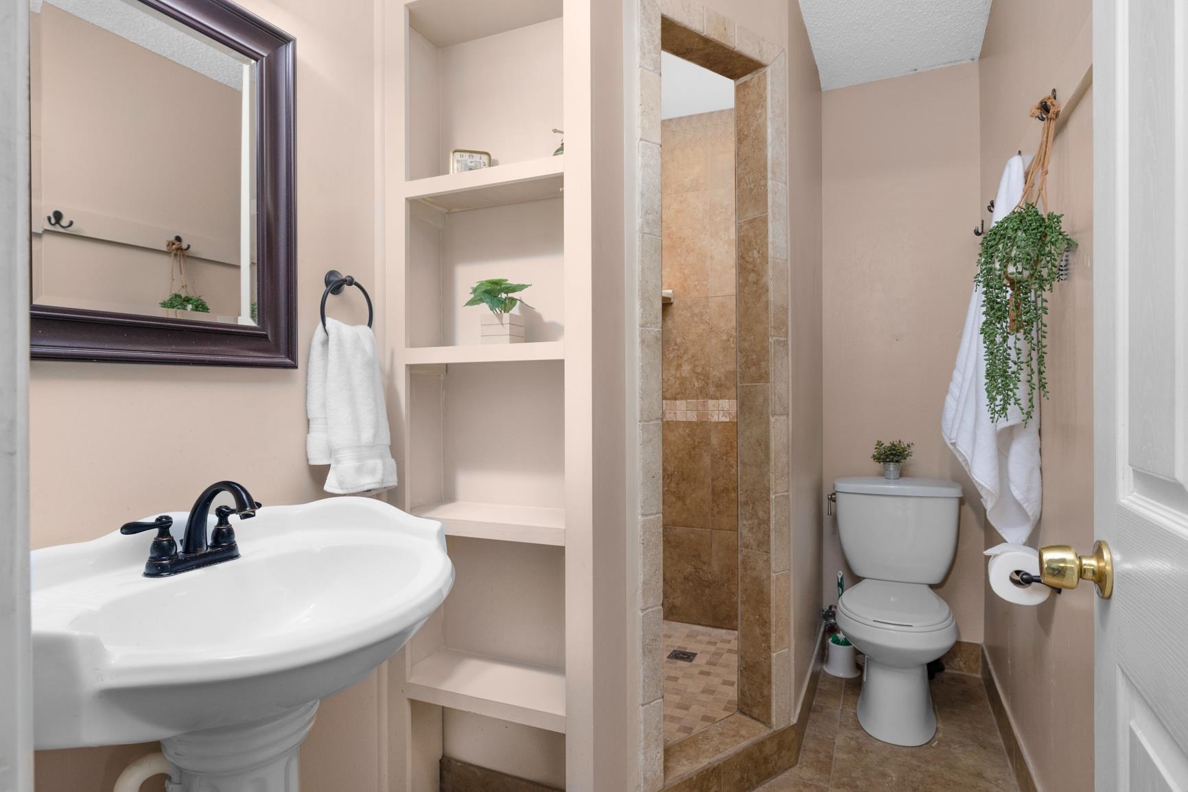 366 Adkins Road Burlison, TN 38015 - Photo 11 of 20 Compact bathroom featuring a pedestal sink with a dark bronze faucet, a framed mirror, built-in shelving, a toilet, and a tiled shower stall