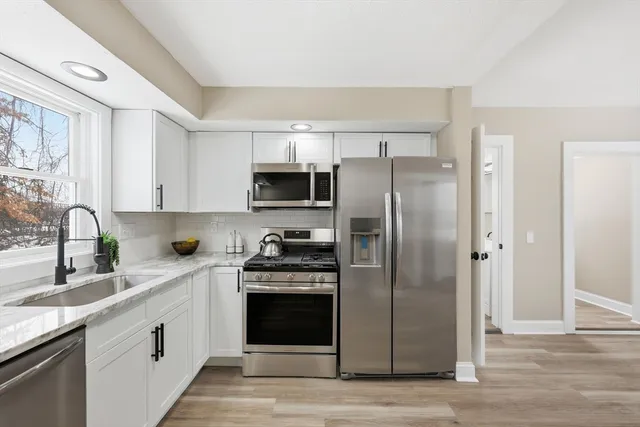 a kitchen with stainless steel appliances granite countertop a refrigerator stove a sink and white cabinets with wooden floor