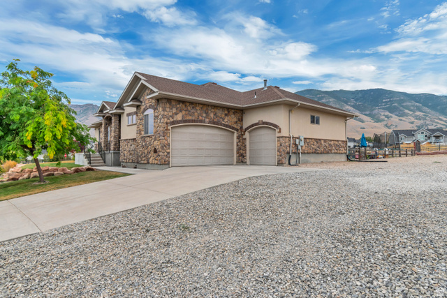 7296 Ridge Road Lake Point, UT 84074 - Photo 4 of 54 Stone and stucco exterior with a multi-car garage, concrete driveway, and gravel parking area