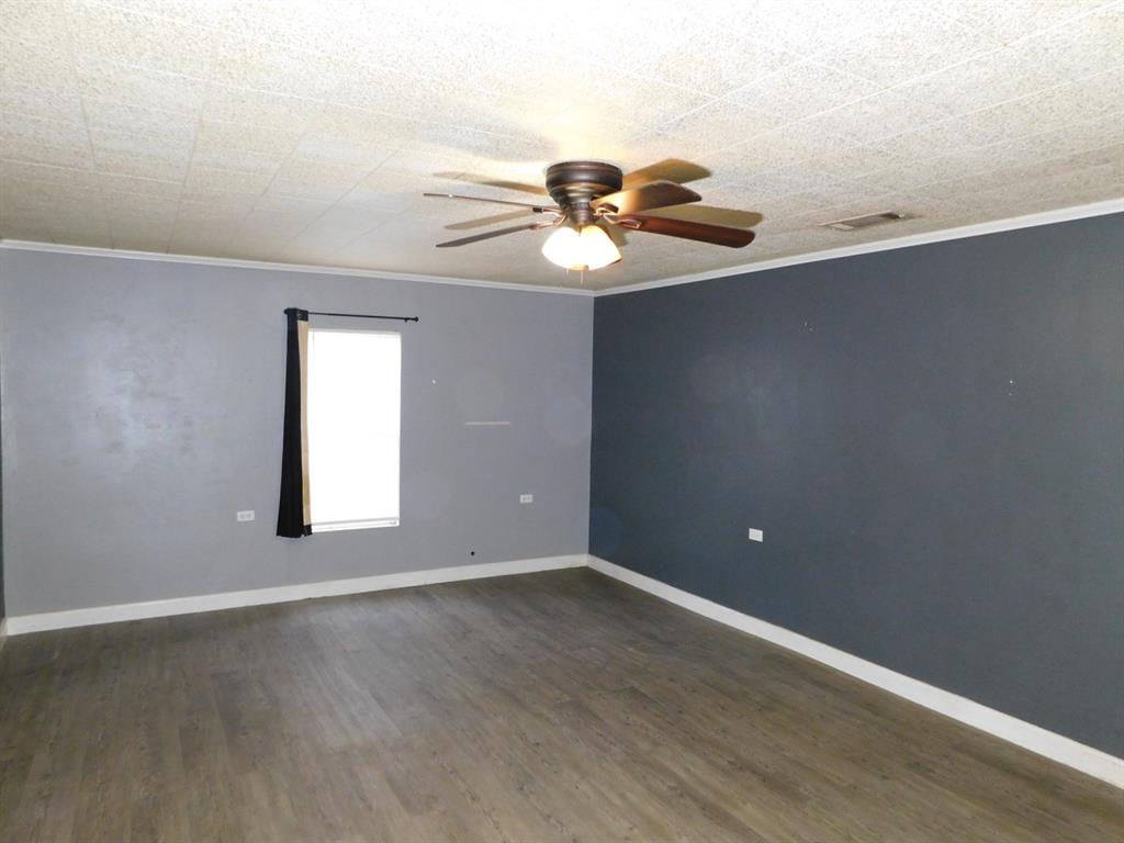 901 North Arkansas Street Springhill, LA 71075 - Photo 14 of 26 Empty room with dark wood finished floors, baseboards, ornamental molding, and a ceiling fan