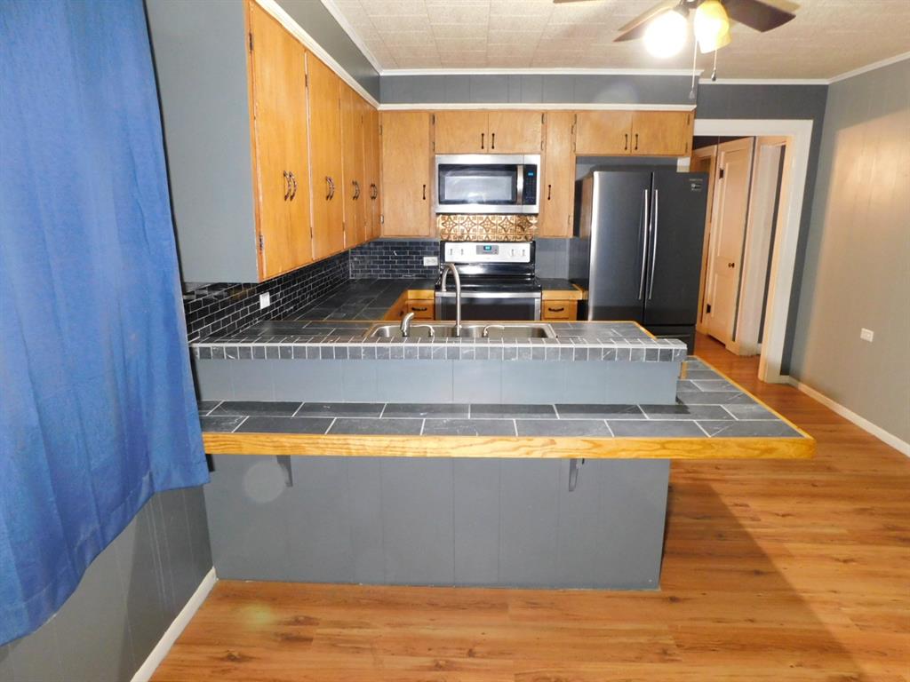 901 North Arkansas Street Springhill, LA 71075 - Photo 26 of 26 Kitchen featuring light wood-type flooring, stainless steel appliances, decorative backsplash, tile countertops, and a peninsula