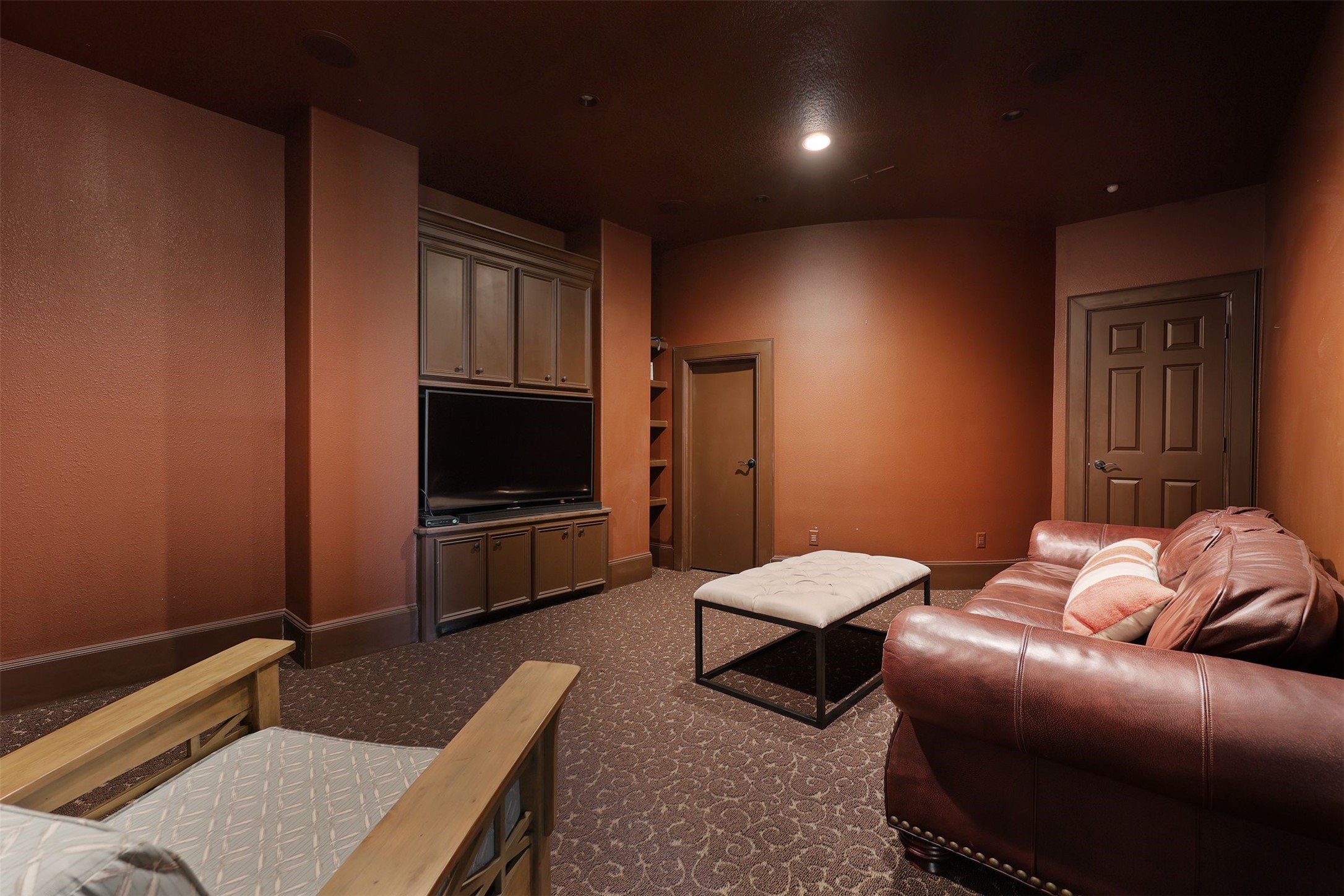 10896 Decatur Street Willis, TX 77318 - Photo 45 of 50 This cozy media room, with its warm, dark walls and plush carpeting, features a large built-in TV cabinet, inviting seating, and a simple ottoman—perfect for movie nights or unwinding in style.