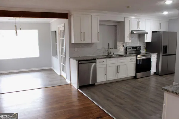 a kitchen with stainless steel appliances granite countertop a refrigerator a stove a sink and white cabinets with wooden floor
