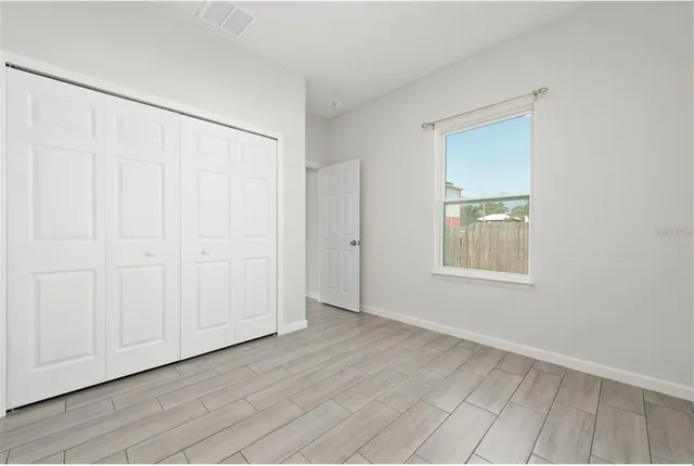 an empty room with wooden floor closet and windows