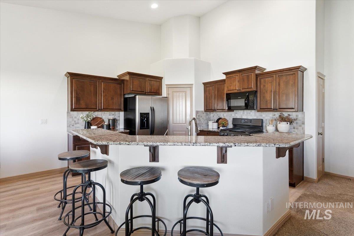 1183 North Buffalo Way Middleton, ID 83644 - Photo 11 of 47 Kitchen featuring a breakfast bar with granite-style countertops, wood cabinetry, stainless steel appliances, and a tiled backsplash