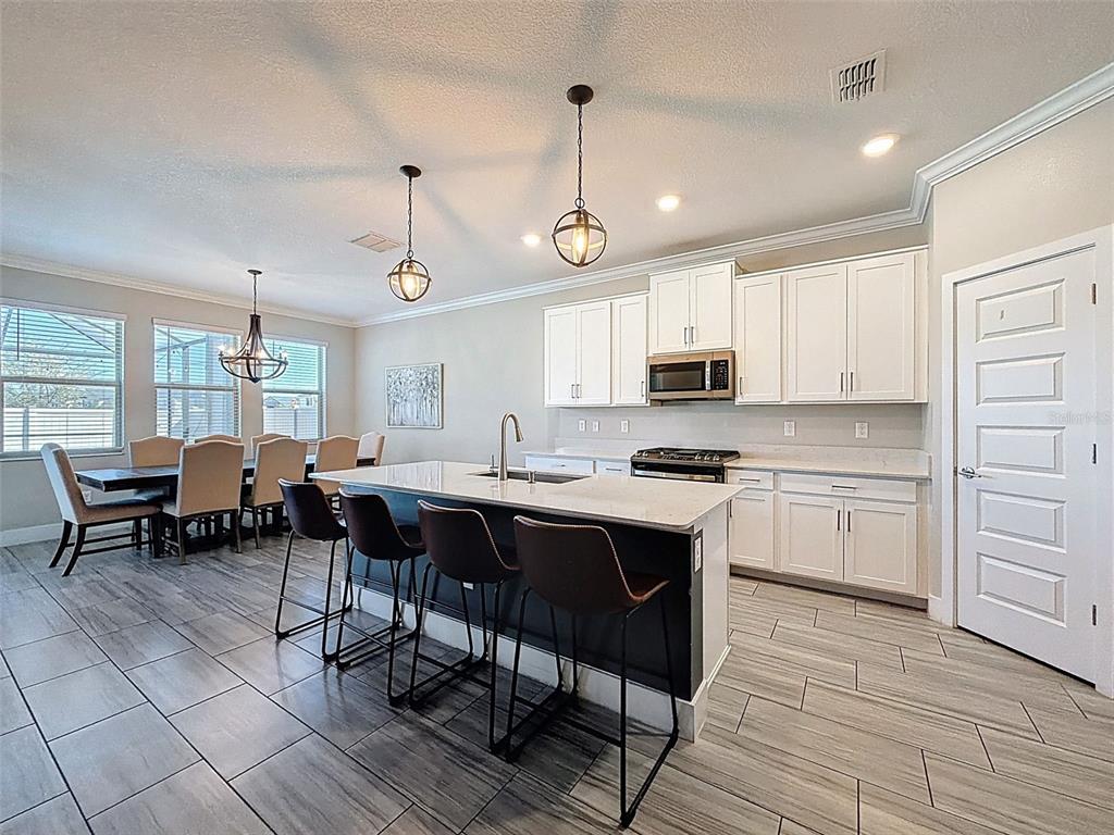 8124 Olympic Stone Circle Trinity, FL 34655 - Photo 14 of 75 a open kitchen with stainless steel appliances granite countertop a stove a sink dishwasher a dining table and chairs with wooden floor